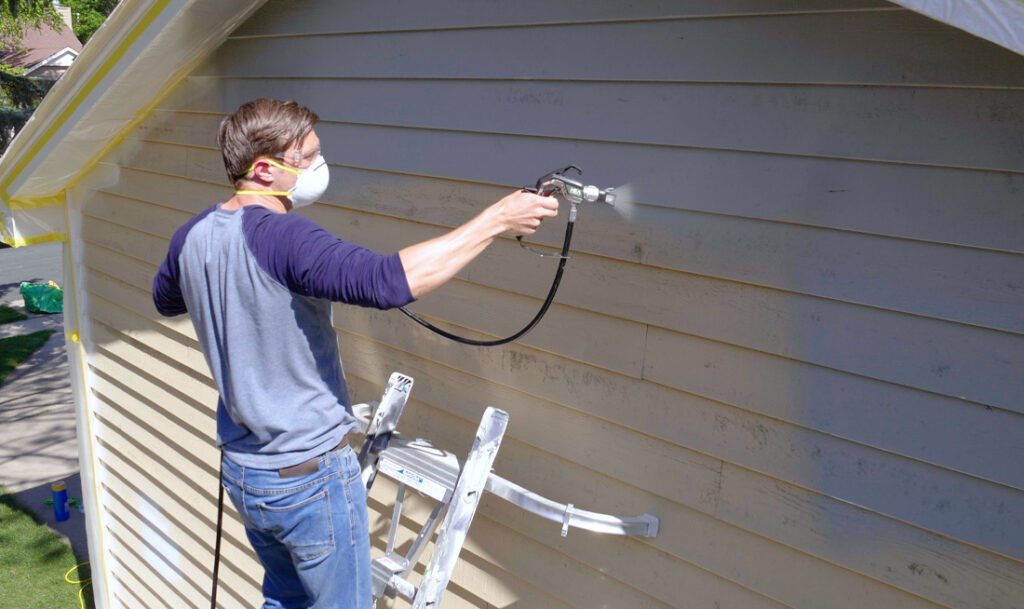 Painter in protective mask using a paint sprayer on a wall